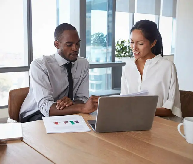 Two people sitting at a table with a laptop