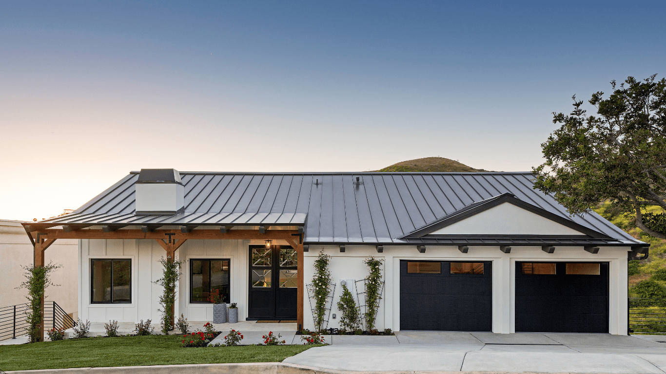 A white house with black garage doors and a metal roof.